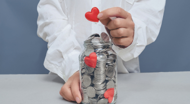 Tarro lleno de monedas con corazones rojos, representando una donación
